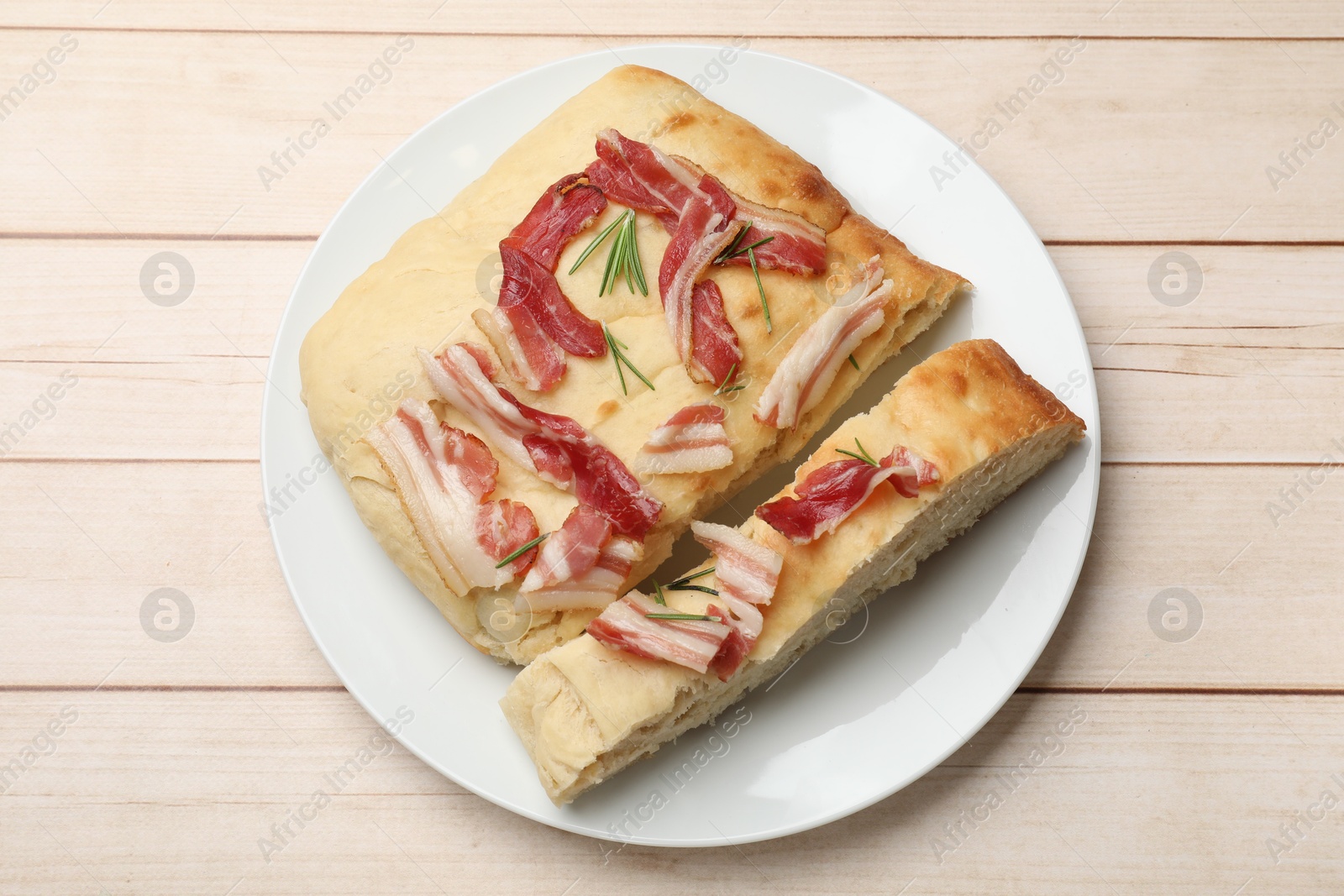 Photo of Pieces of delicious focaccia bread with bacon and rosemary on wooden table, top view