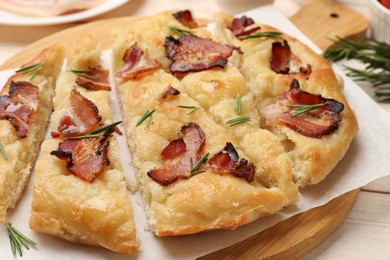 Photo of Slices of delicious focaccia bread with bacon and rosemary on table, closeup