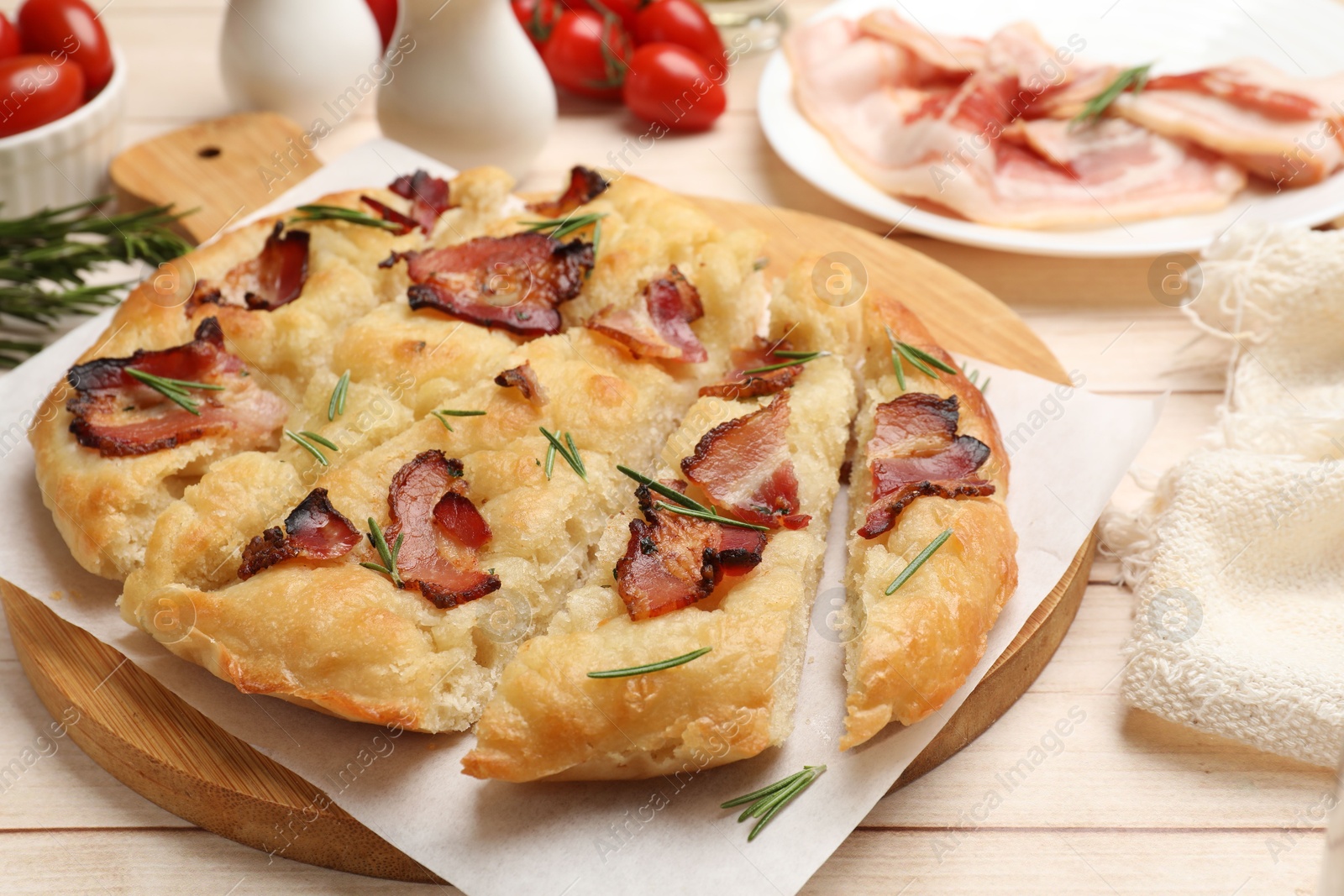 Photo of Slices of delicious focaccia bread with bacon and rosemary on wooden table, closeup