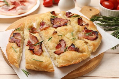 Photo of Slices of delicious focaccia bread with bacon and rosemary on wooden table, closeup