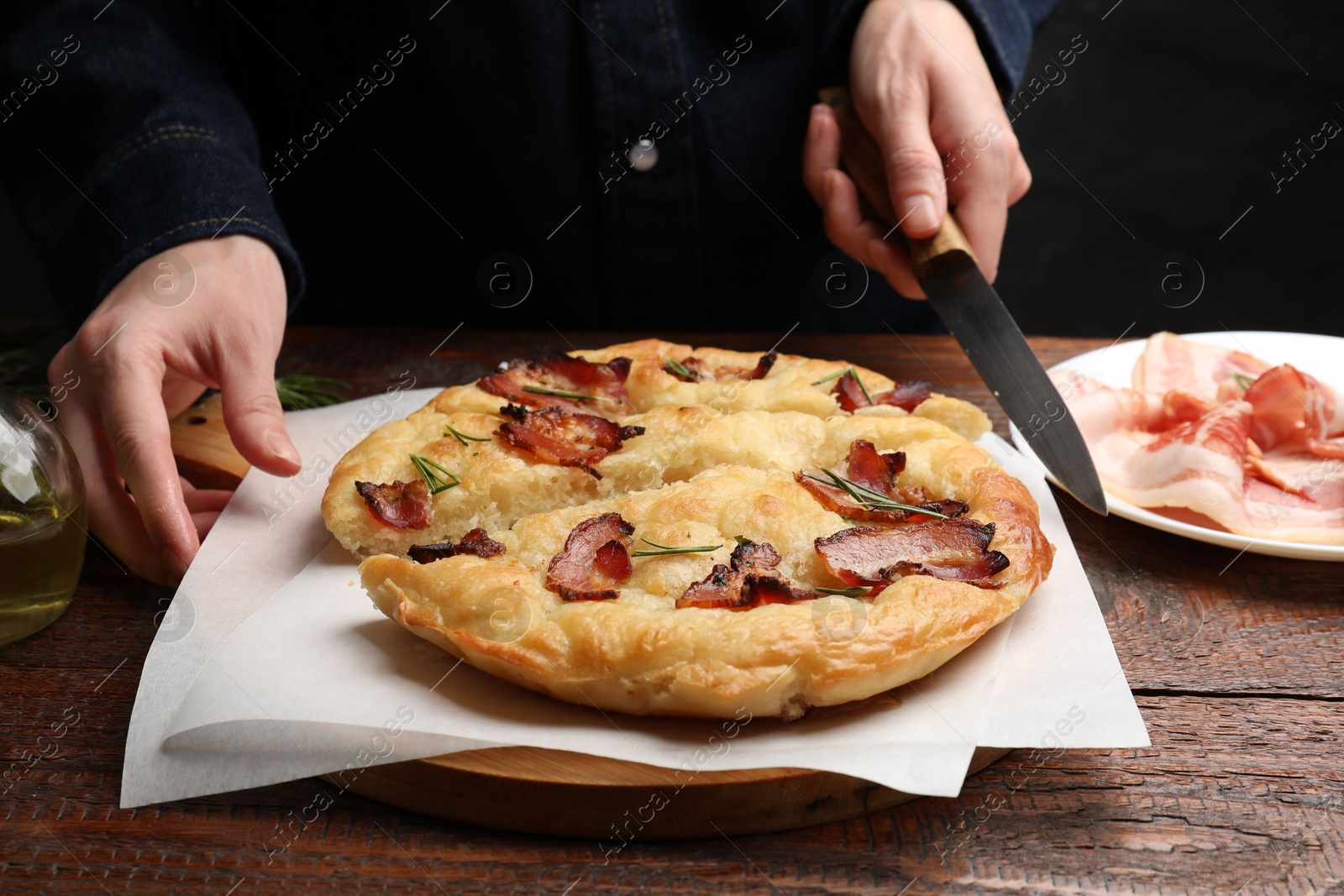 Photo of Woman cutting delicious focaccia bread at wooden table, closeup