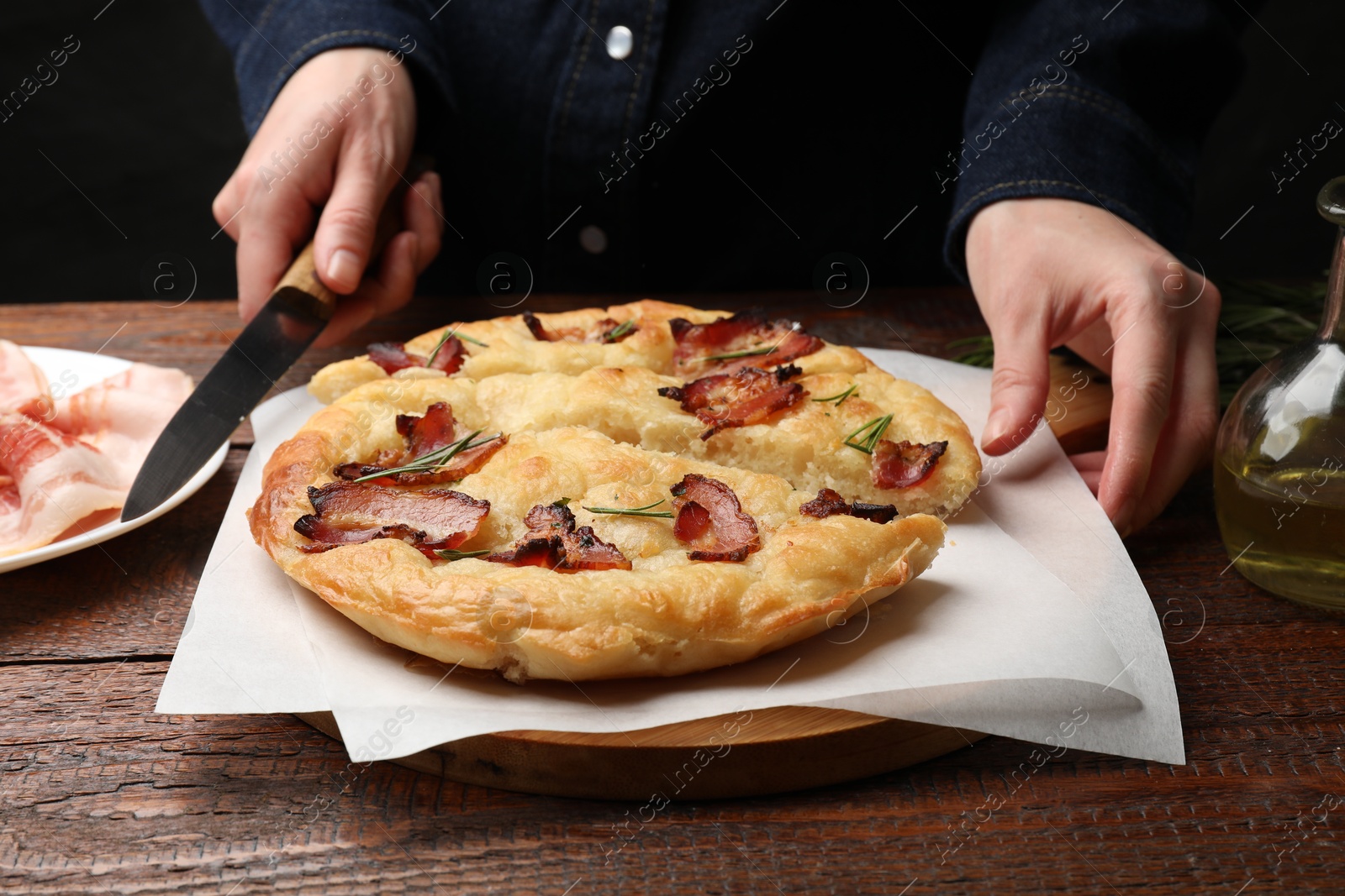 Photo of Woman cutting delicious focaccia bread at wooden table, closeup