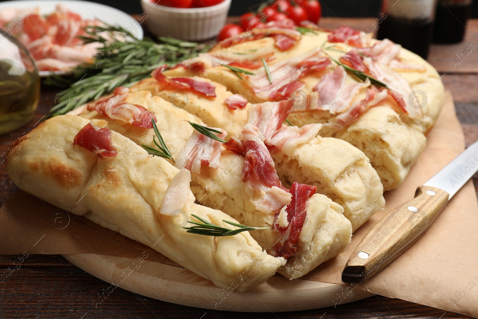 Photo of Slices of delicious focaccia bread with bacon, rosemary and knife on wooden table, closeup