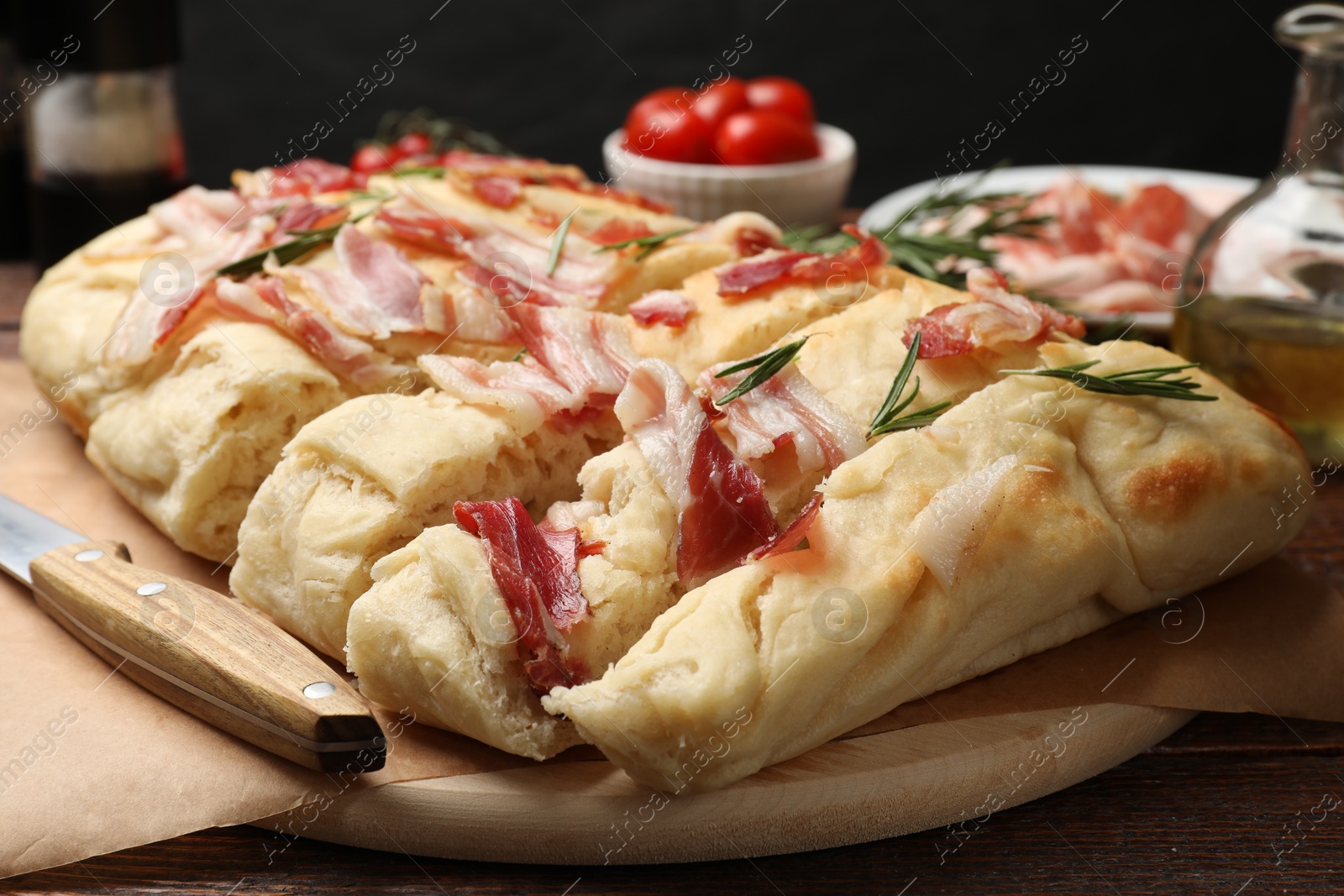 Photo of Slices of delicious focaccia bread with bacon, rosemary and knife on wooden table, closeup