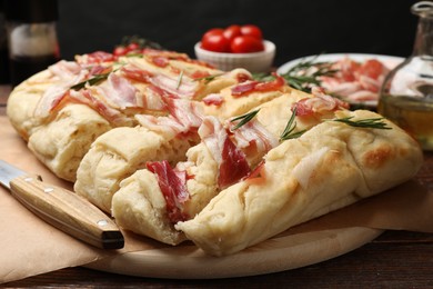 Photo of Slices of delicious focaccia bread with bacon, rosemary and knife on wooden table, closeup