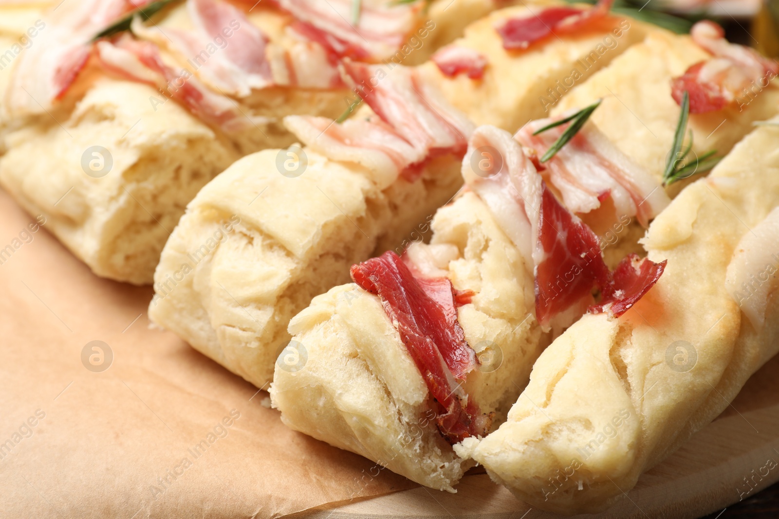 Photo of Slices of delicious focaccia bread with bacon and rosemary on table, closeup