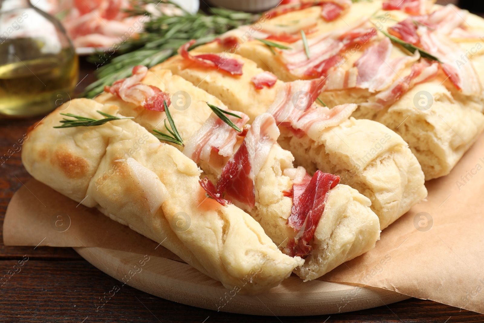 Photo of Slices of delicious focaccia bread with bacon and rosemary on wooden table, closeup