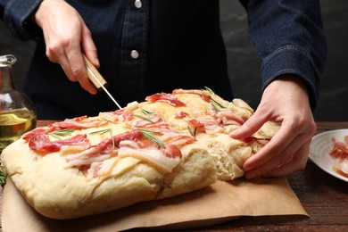 Photo of Woman cutting delicious focaccia bread at wooden table, closeup