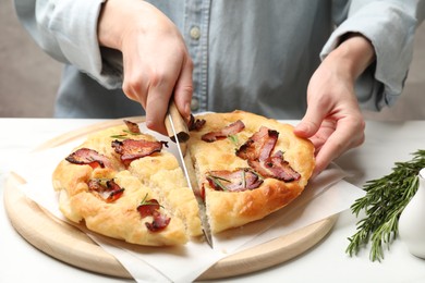 Photo of Woman cutting delicious focaccia bread at white table, closeup