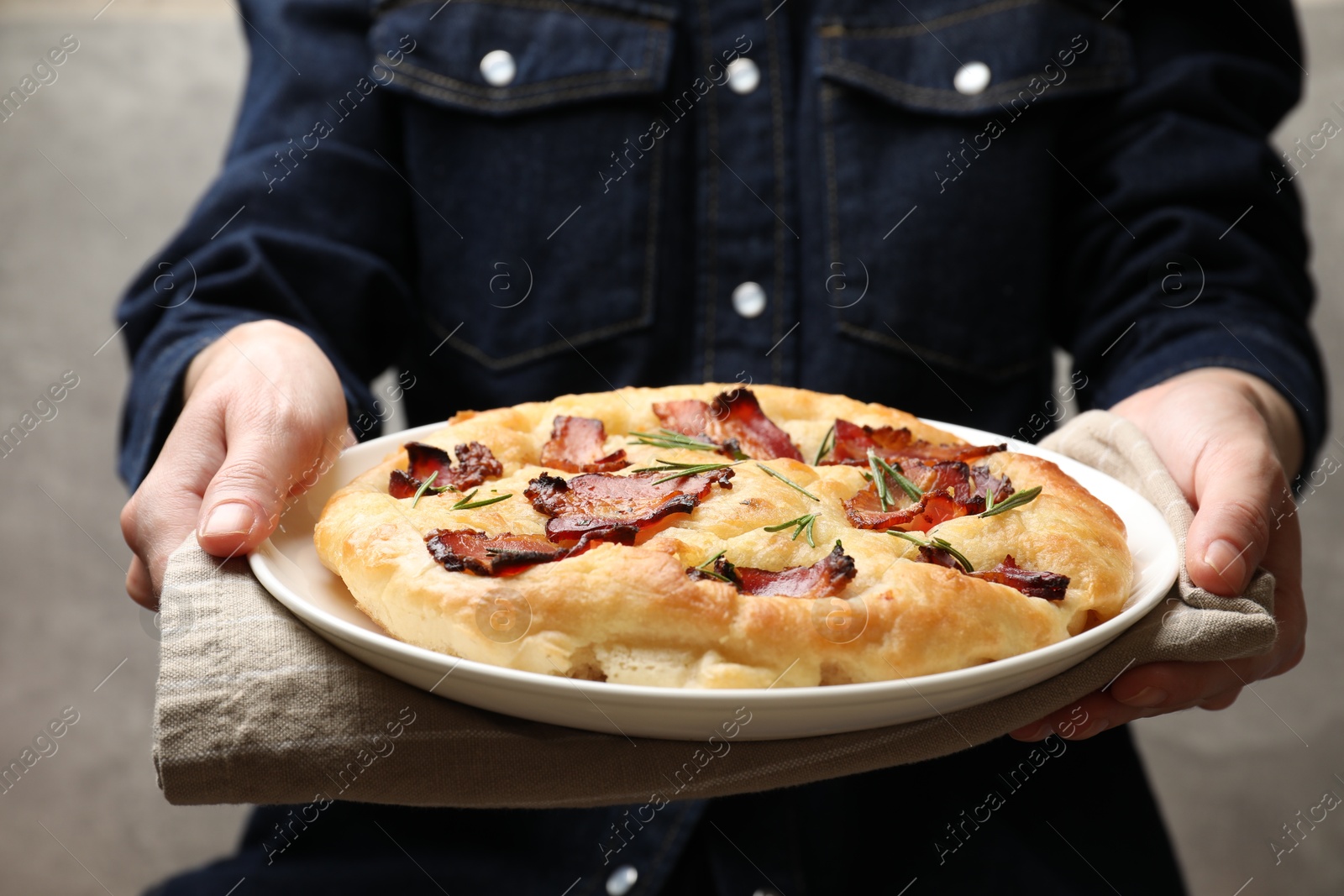 Photo of Woman holding delicious focaccia bread with bacon and rosemary on grey background, closeup