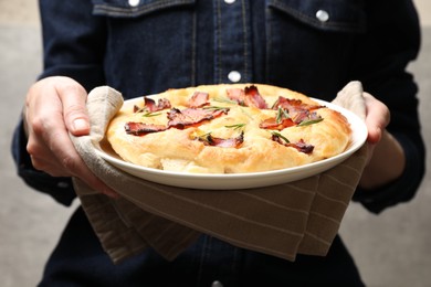 Photo of Woman holding delicious focaccia bread with bacon and rosemary on grey background, closeup