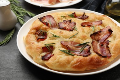 Photo of Delicious focaccia bread with bacon and rosemary on black table, closeup