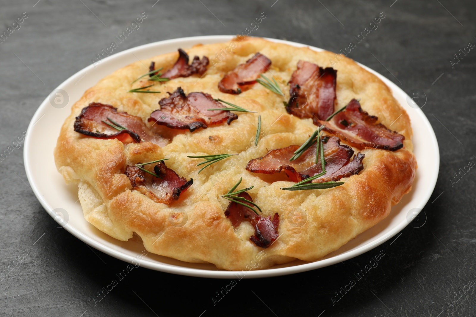 Photo of Delicious focaccia bread with bacon and rosemary on black table, closeup