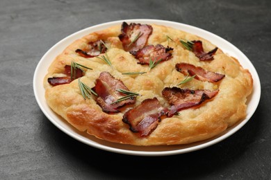 Photo of Delicious focaccia bread with bacon and rosemary on black table, closeup