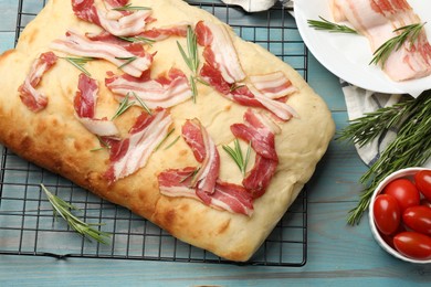 Photo of Delicious focaccia bread with bacon, rosemary and tomatoes on light blue wooden table, flat lay