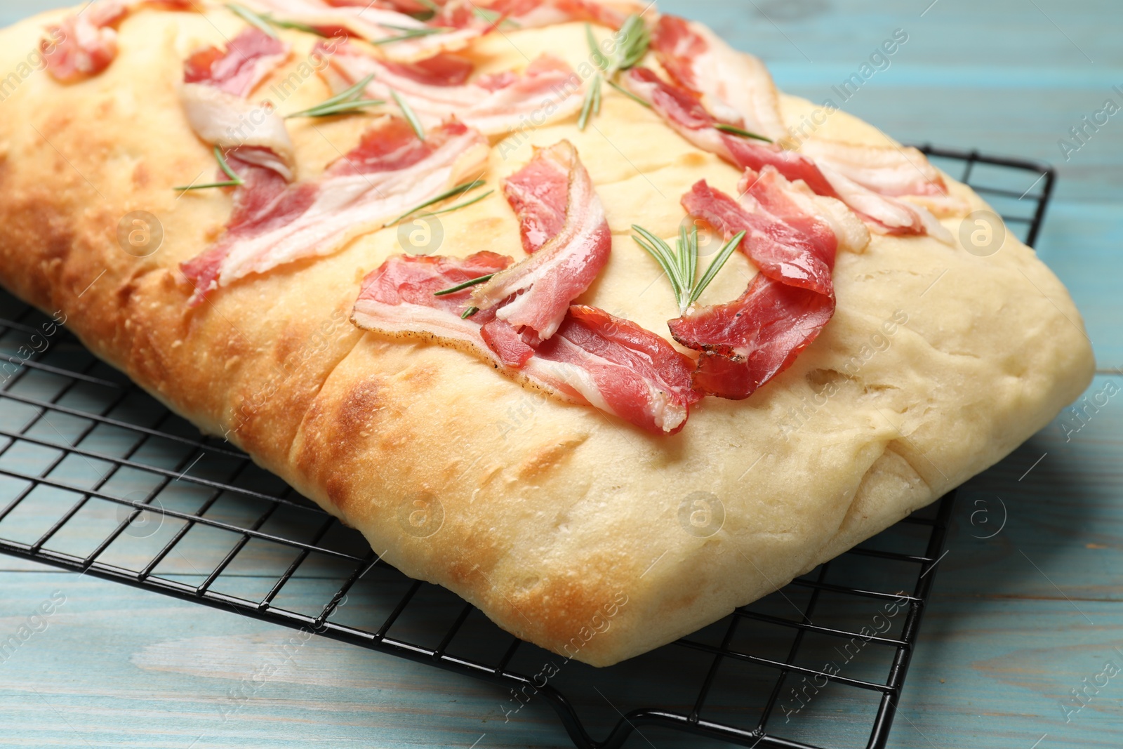 Photo of Delicious focaccia bread with bacon and rosemary on light blue wooden table, closeup