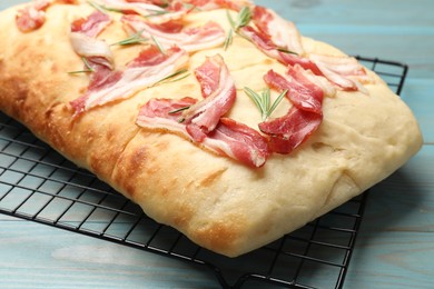 Photo of Delicious focaccia bread with bacon and rosemary on light blue wooden table, closeup