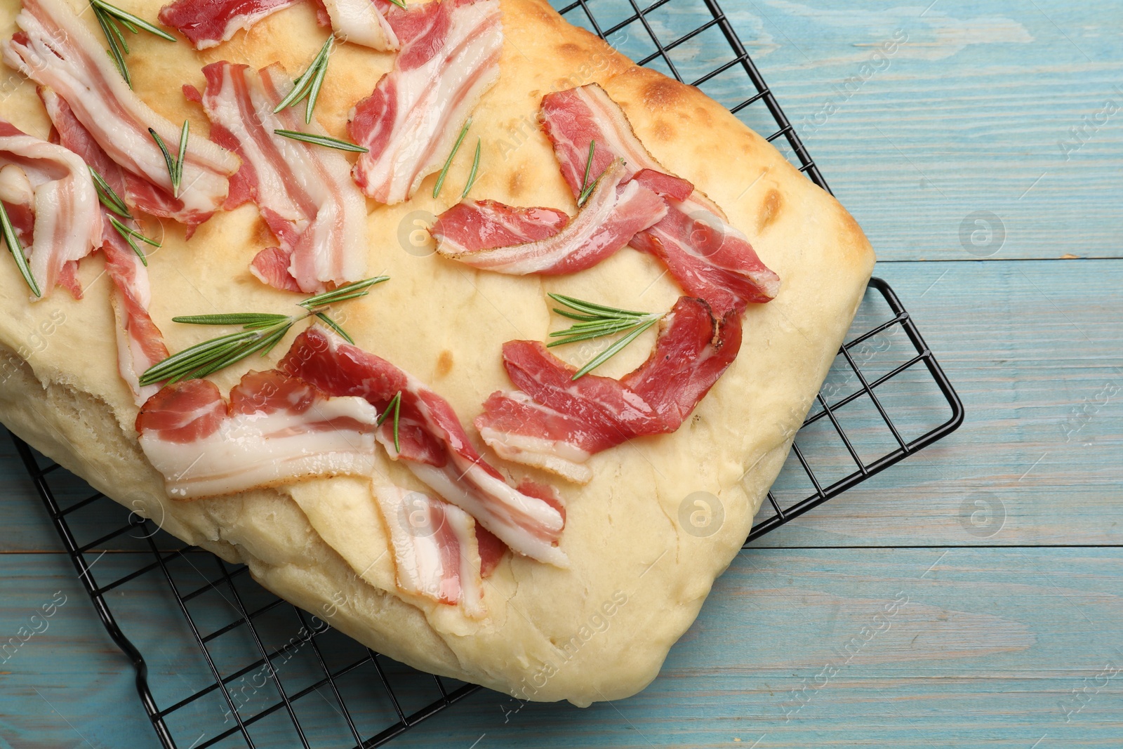 Photo of Delicious focaccia bread with bacon and rosemary on light blue wooden table, top view