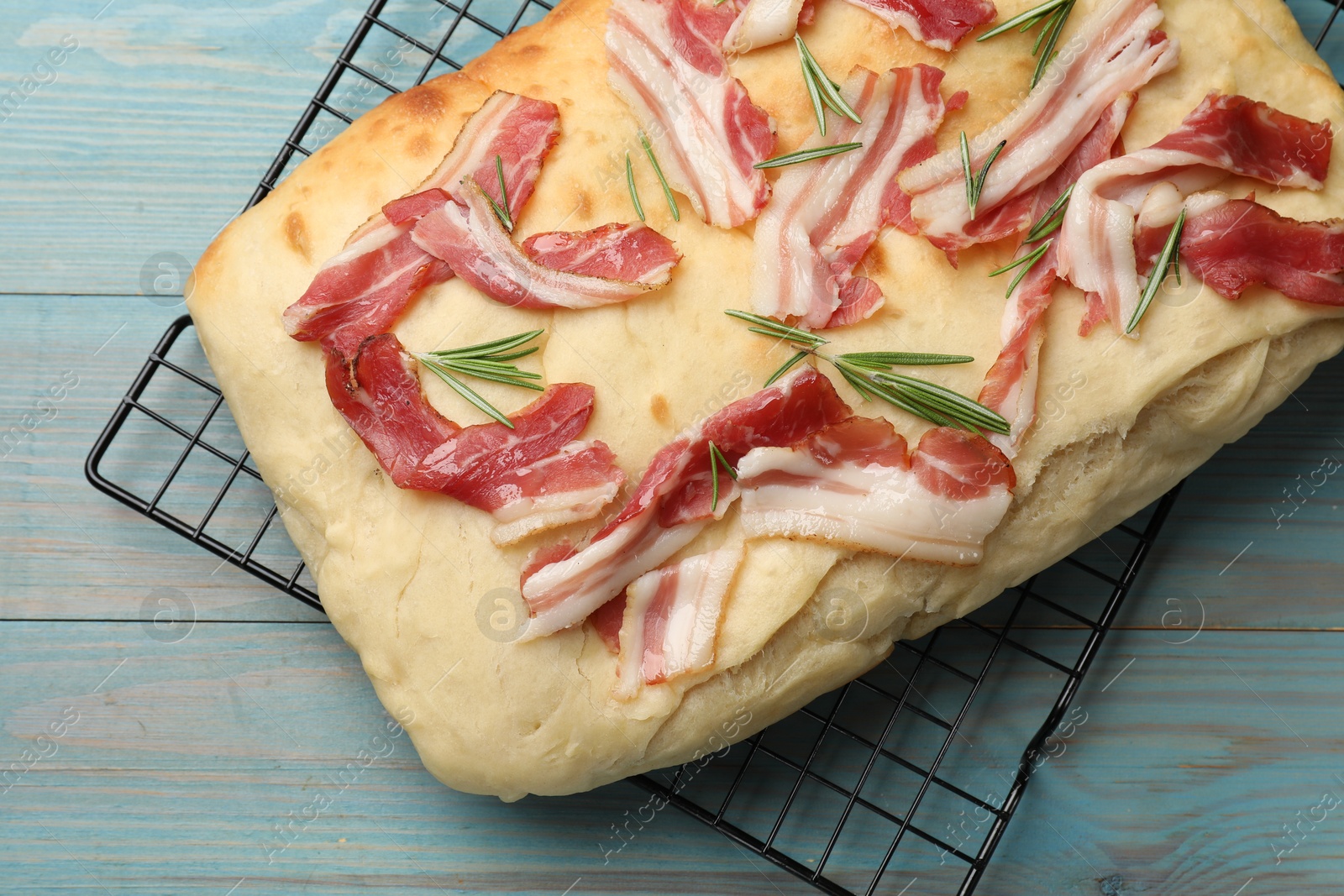 Photo of Delicious focaccia bread with bacon and rosemary on light blue wooden table, top view