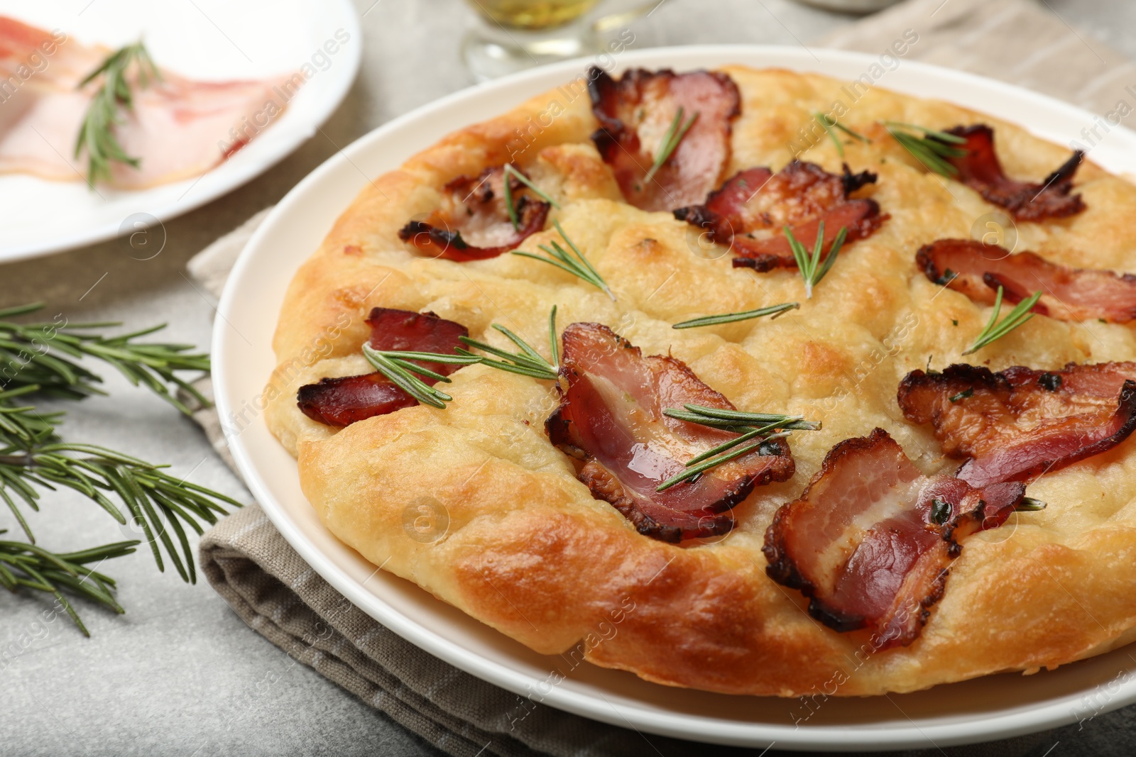 Photo of Delicious focaccia bread with bacon and rosemary on light grey table, closeup