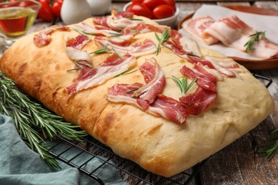 Photo of Delicious focaccia bread with bacon, rosemary, oil and tomatoes on wooden table, closeup