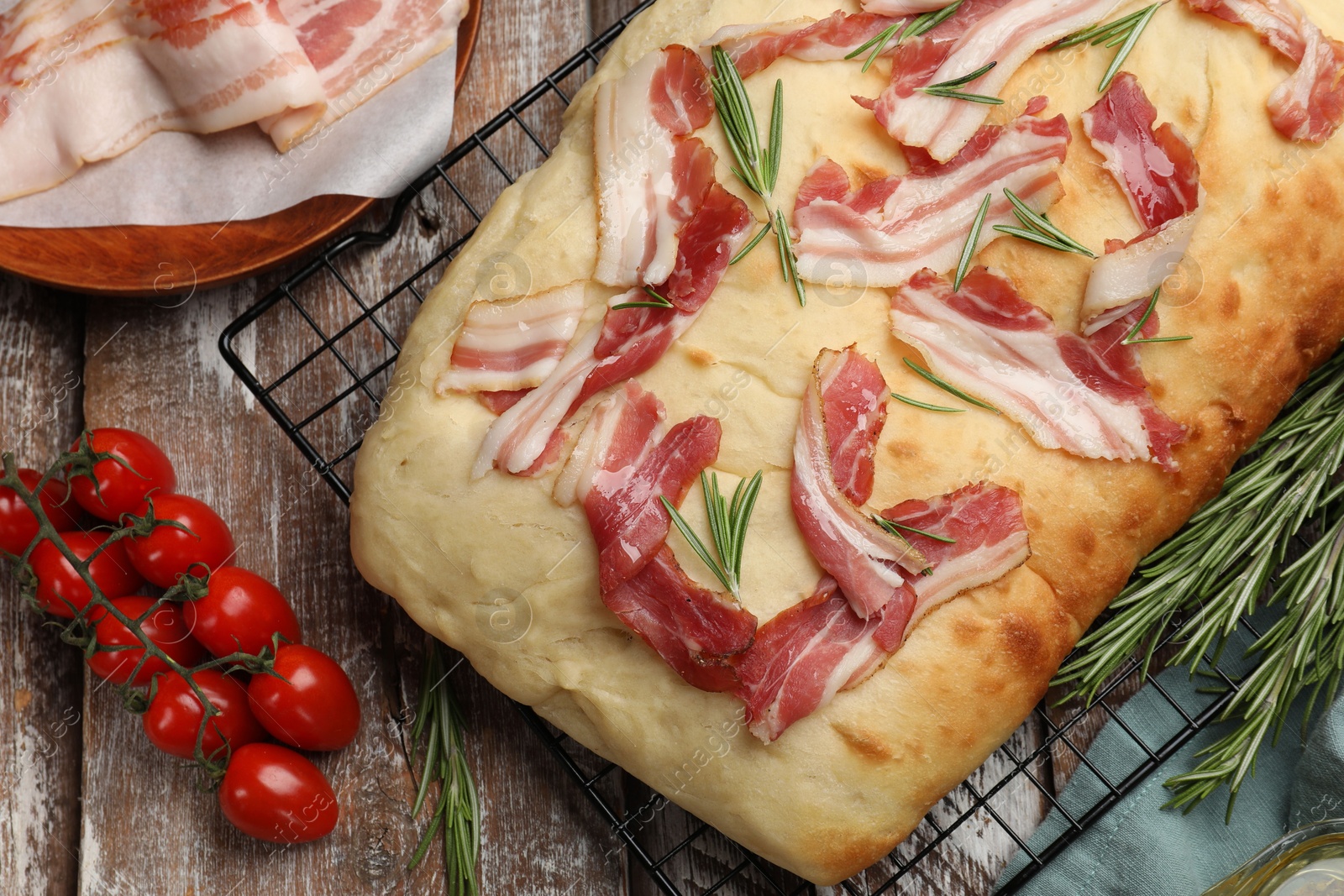 Photo of Delicious focaccia bread with bacon, rosemary and tomatoes on wooden table, flat lay