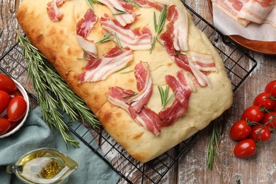 Photo of Delicious focaccia bread with bacon, rosemary, oil and tomatoes on wooden table, flat lay