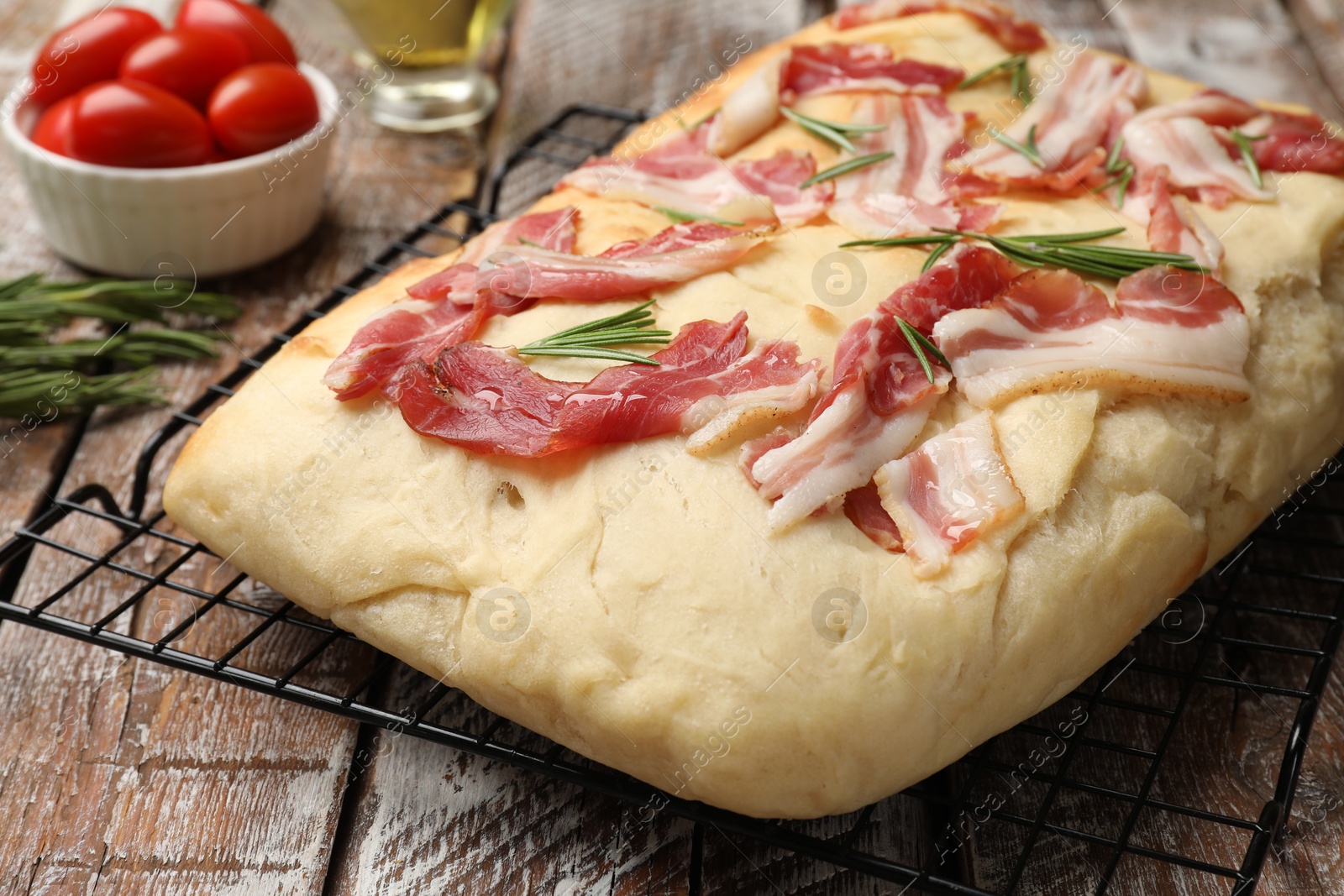 Photo of Delicious focaccia bread with bacon, rosemary and tomatoes on wooden table, closeup