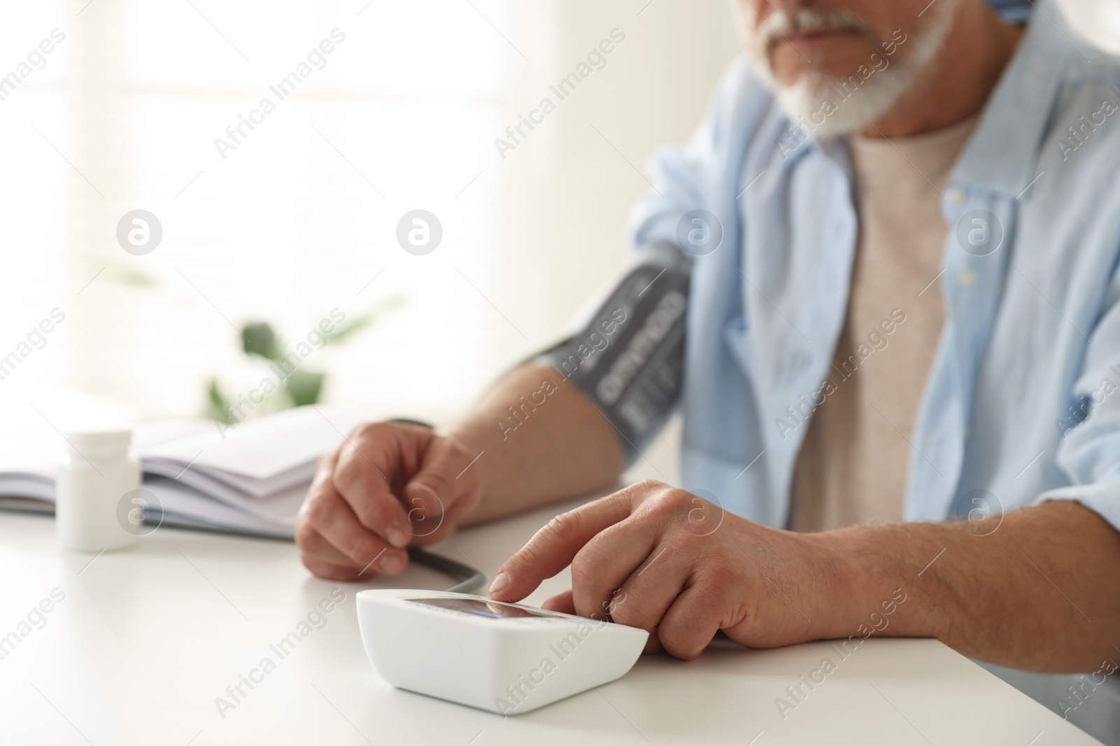 Photo of Senior man measuring blood pressure at table indoors, closeup