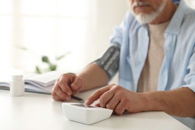 Photo of Senior man measuring blood pressure at table indoors, closeup