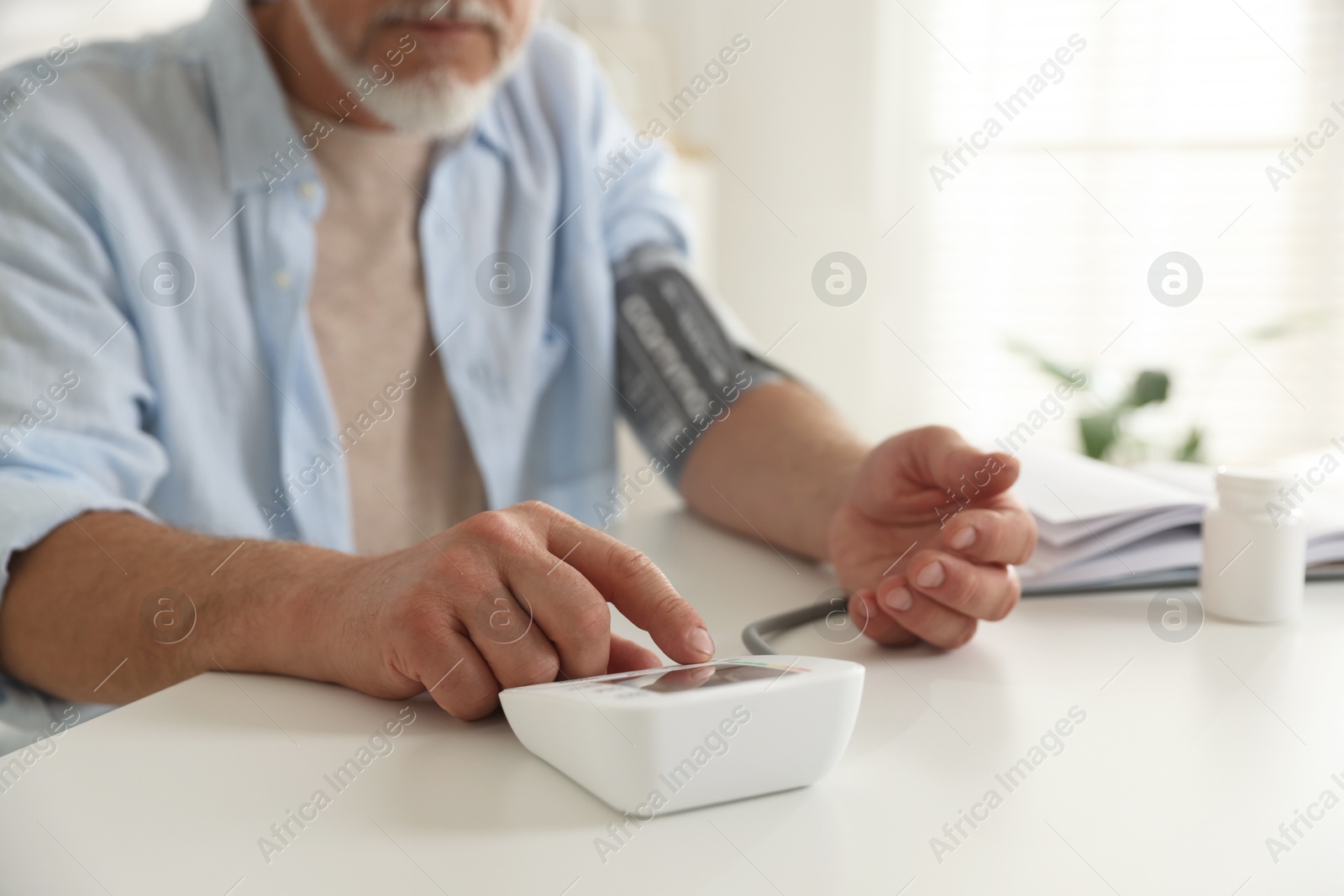 Photo of Senior man measuring blood pressure at table indoors, closeup