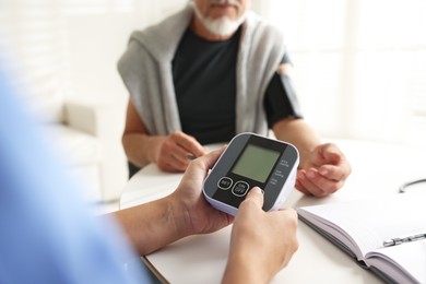 Photo of Doctor measuring patient's blood pressure at table indoors, closeup