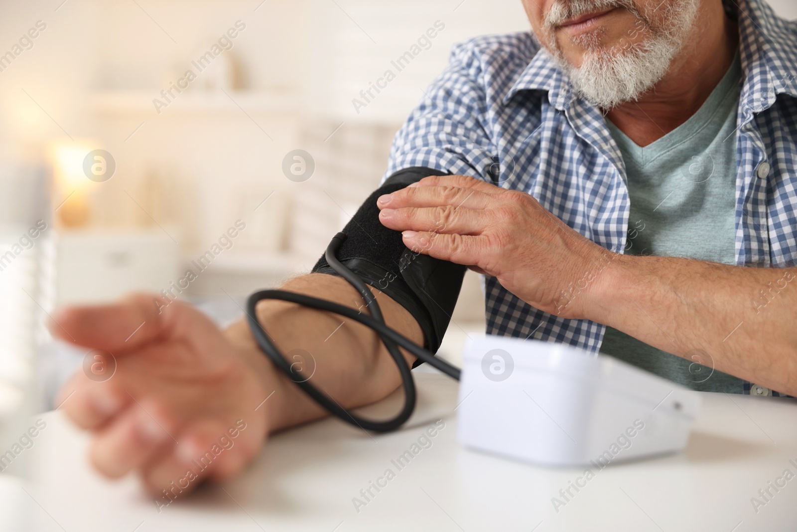 Photo of Senior man measuring blood pressure at table indoors, closeup