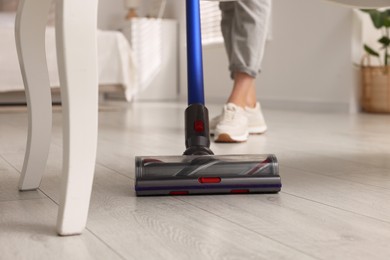 Photo of Woman cleaning floor with cordless vacuum cleaner at home, closeup