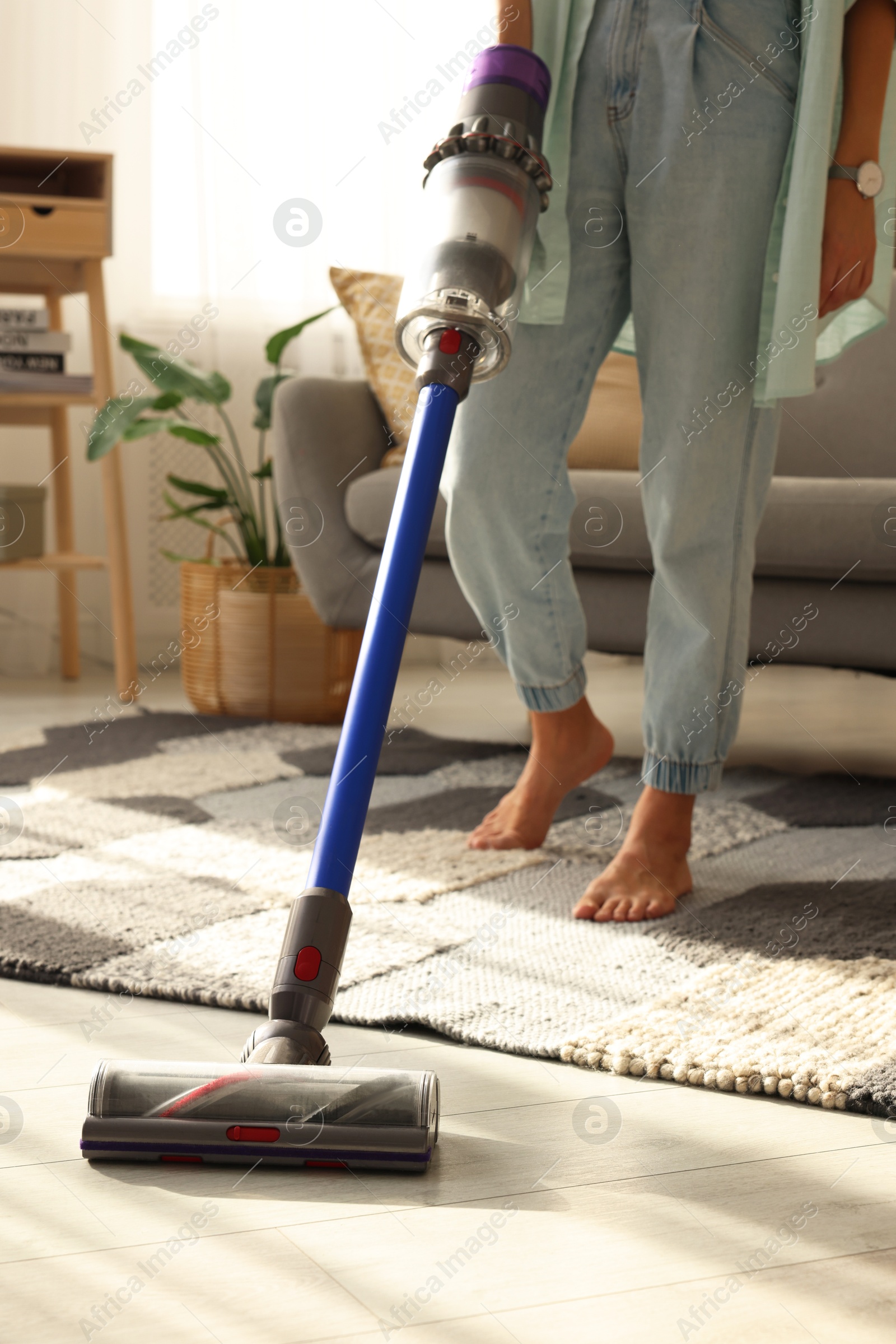 Photo of Woman cleaning floor with cordless vacuum cleaner at home, closeup