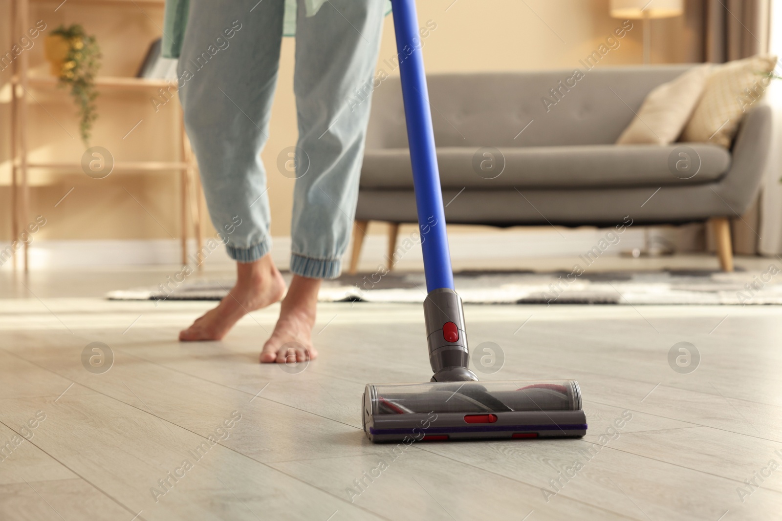 Photo of Woman cleaning floor with cordless vacuum cleaner at home, closeup