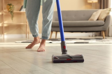 Photo of Woman cleaning floor with cordless vacuum cleaner at home, closeup