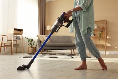 Photo of Woman cleaning floor with cordless vacuum cleaner at home, closeup