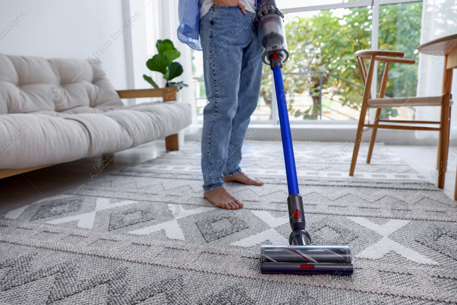 Photo of Man cleaning rug with cordless vacuum cleaner at home, closeup