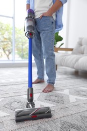 Photo of Man cleaning rug with cordless vacuum cleaner at home, closeup