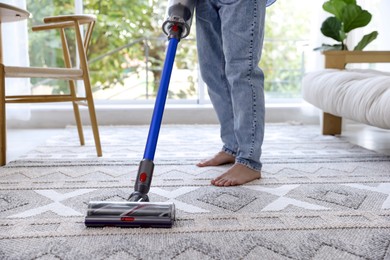 Photo of Man cleaning rug with cordless vacuum cleaner at home, closeup