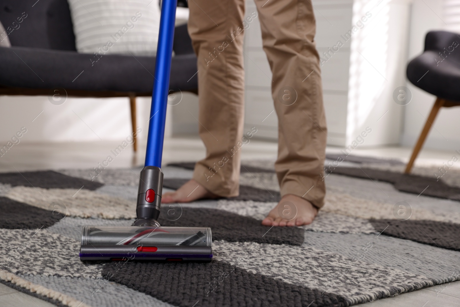 Photo of Man cleaning rug with cordless vacuum cleaner at home, closeup