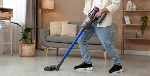 Photo of Man cleaning floor with cordless vacuum cleaner at home, closeup