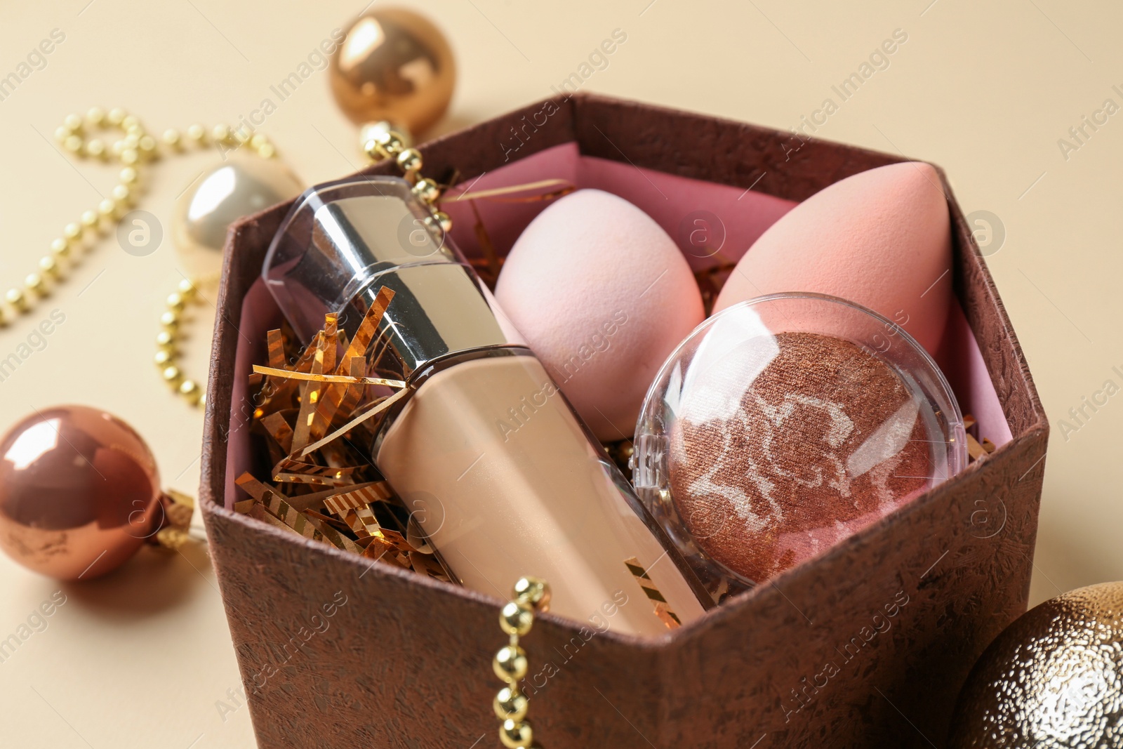 Photo of Cosmetic products in gift box and Christmas balls on beige background, closeup