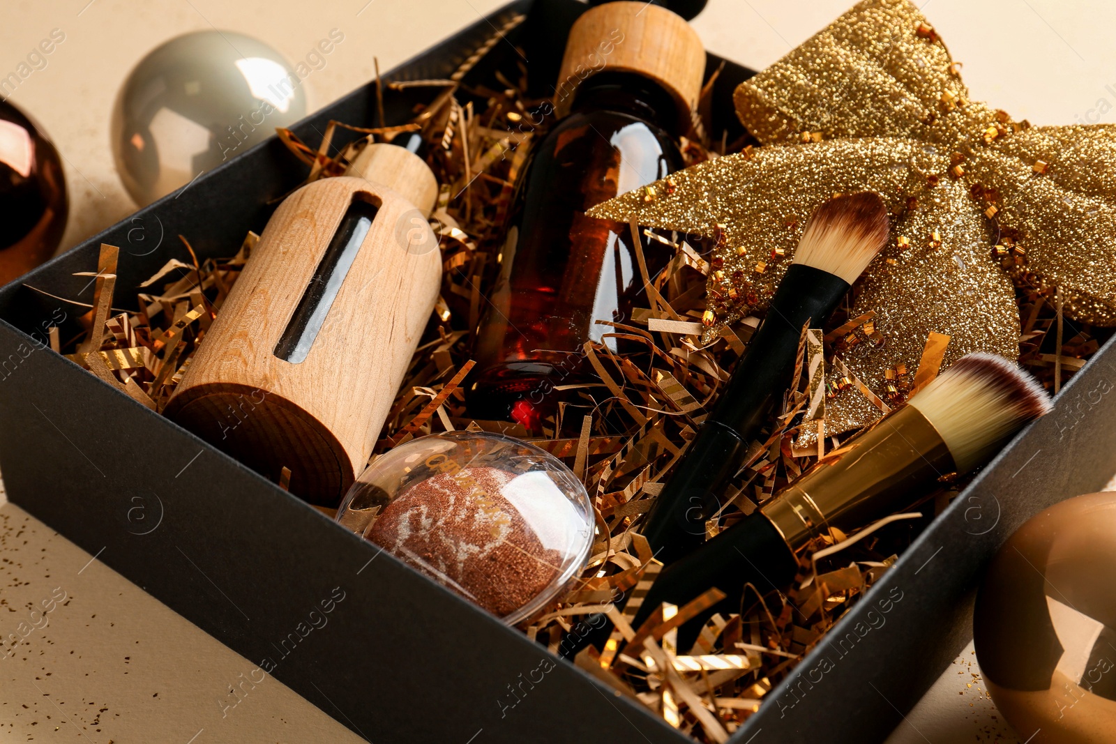 Photo of Christmas gift box with cosmetic products and festive balls on beige background, closeup