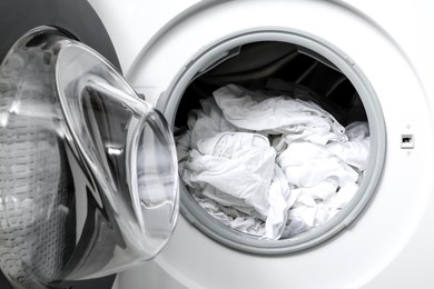 Photo of Open washing machine with clean clothes, closeup