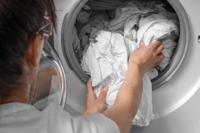 Photo of Woman taking clean clothes out of washing machine, closeup