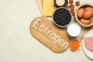 Photo of Wooden board with word Estrogen and different fresh products on light textured table, flat lay. Space for text