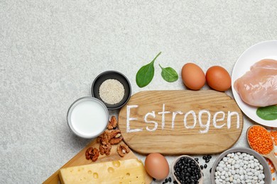 Photo of Wooden board with word Estrogen and different fresh products on light textured table, flat lay. Space for text