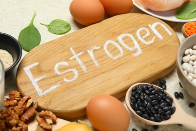 Photo of Wooden board with word Estrogen and different fresh products on light table